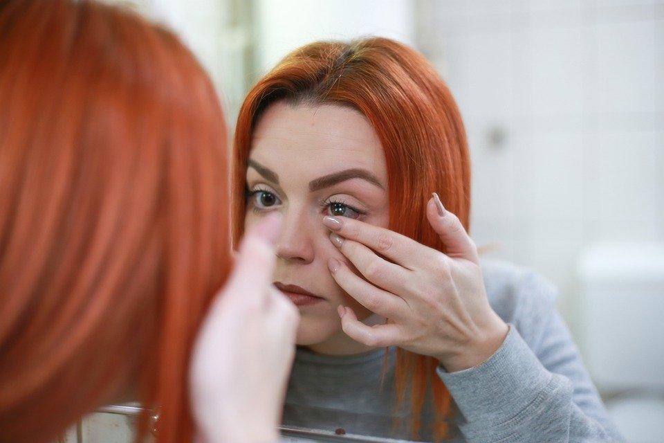 Una chica se pone una lentilla frente al espejo
